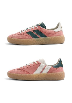 Paire de baskets en daim rose avec semelles en gomme, l'une avec des rayures vert foncé et l'autre avec des rayures blanches, toutes deux avec des lacets blancs.