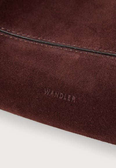 Burgundy mockaskmaterial med en slät yta, med en subtil sömdetalj och det ingraverade "WANDLER"-logotypen på ena sidan.