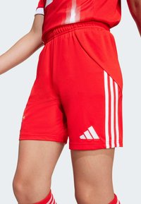 Červené športové šortky s bielymi bočnými pruhmi, elastickým pásom a logom Adidas. Vyrobené z hladkej, ľahkej látky s priliehajúcim strihom.