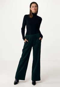 Svart polotröja i kombination med vida, mörkgröna cordbyxor med elastisk midja och sidofickor, kompletterat med svarta klackar.