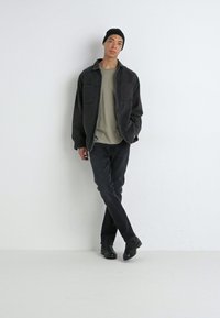 Chaqueta de denim negra sobre una camiseta gris clara, combinada con jeans negros y botines negros. El modelo está de pie contra un fondo blanco liso.