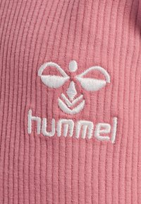 Rosa ribbad tyg med en vit broderad logotyp med en symmetrisk design och texten "hummel" längst ner. Tyget är mjukt och strukturerat.