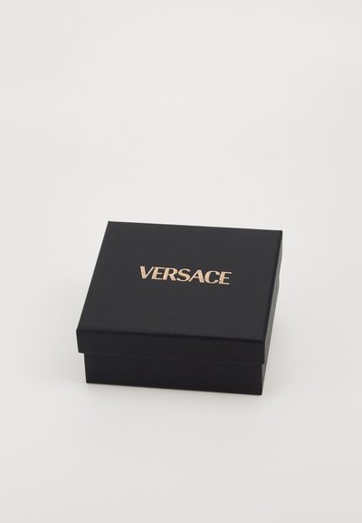 Melns kartona kastē ar matētu apdari, ar zelta "VERSACE" logo uz vāka. Kvadrātveida forma, gluda tekstūra, minimālisma dizains.