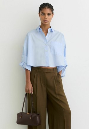 Šviesiai mėlyna trumpinta marškinėliai su krūtine kišene, derinami su aukšto liemens alyvuoginių žalių kelnių. Ruda rankinė su trumpomis rankenomis.