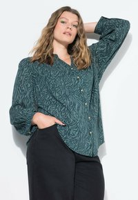 Camicia verde con stampa animale, con maniche lunghe, una vestibilità morbida e bottoni dorati. Abbinata a pantaloni neri.