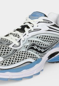 Αθλητικό παπούτσι Saucony σε λευκό και μαύρο με μπλε λεπτομέρειες, επάνω μέρος από δίχτυ, λευκά κορδόνια και μαξιλαρωμένη σόλα.