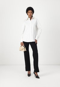 White shirt with a pointed collar, black tailored trousers, black patent heels, and a small beige handbag featuring a signature design.