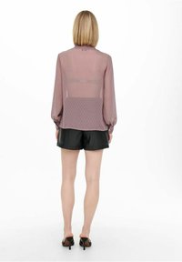 Sheer mauve blouse with long, puffed sleeves and polka dot pattern, paired with black shorts. This view shows the back of the outfit.