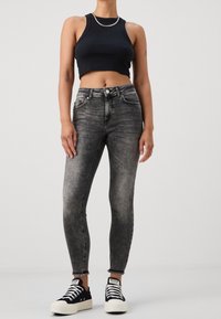 Top corto negro, jeans de mezclilla grises de cintura alta con un acabado desgastado, dobladillo deshilachado y zapatillas negras de corte bajo con suelas blancas.