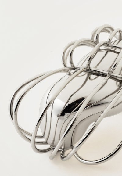 Ασημένιο βραχιόλι σε σχήμα κλουβιού με λείες, κυρτές ράβδους που δημιουργούν έναν ανοιχτό, αέρινο σχεδιασμό σε λευκό φόντο.