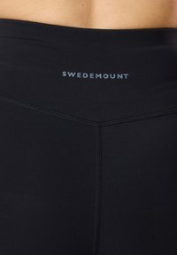 Leggings neri in materiale elasticizzato con una texture liscia, una vita alta e il nome del marchio "SWEDEMOUNT" stampato in azzurro chiaro.