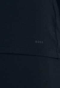 Tessuto blu scuro con il logo "BOSS" stampato in modo discreto vicino al bordo orlato, che mostra dettagli di texture e cucitura.