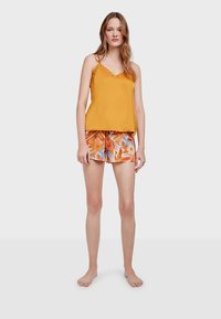 Camiseta de satén amarilla con ribete decorativo, combinada con pantalones cortos de patrón naranja y azul hechos de una tela ligera.