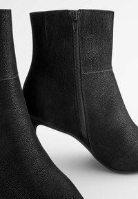 Bottines noires en cuir texturé, dotées d'une fermeture éclair latérale et d'un talon fin, avec un intérieur lisse et des détails de couture minimalistes.