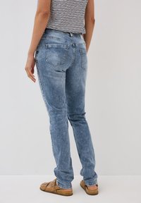 Bleka blå denimjeans med slim fit, med två bakfickor och sömnadsdetaljer längs sömmarna. Bärs med bruna sandaler.