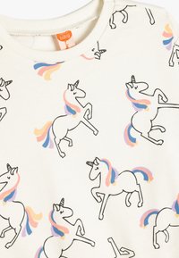 Witte sweatshirt met zwart omlijnde eenhoorns met pastelgekleurde manen in roze, blauw en geel, op een zachte stofoppervlak.