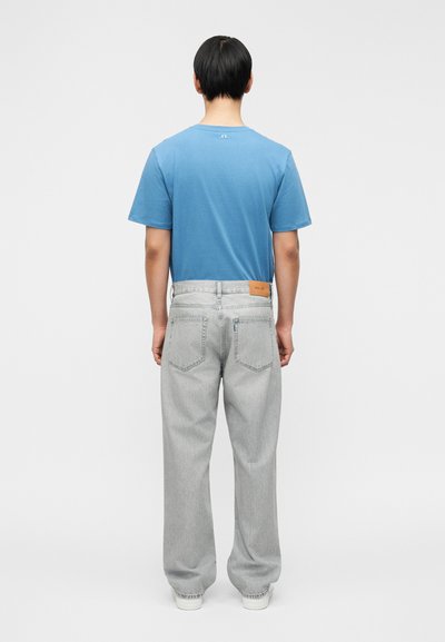 Γαλάζιο βαμβακερό t-shirt με κοντά μανίκια, σε συνδυασμό με ανοιχτό γκρι τζιν παντελόνι φαρδιάς γραμμής που διαθέτει λογότυπο ταμπ στο πίσω μέρος της μέσης.