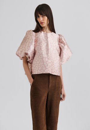 Kortermet, rosa bluse med et subtilt dyreprint, med rund halsutskjæring og puffermer. Kombinert med brune skinnbukser.