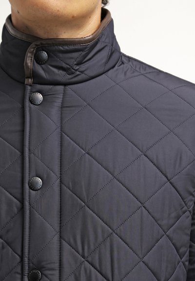 Veste matelassée bleue marine avec un col montant, dotée de boutons pression noirs, d'un motif en losanges et d'accents bruns contrastants le long du col.