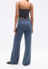 Jasnoniebieskie spodnie typu wide-leg o gładkiej fakturze, z tylnymi kieszeniami. Połączone z ciemnoszarym, prążkowanym crop topem.