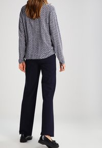 Blusa a maniche lunghe a motivo navy con vestibilità comoda, abbinata a pantaloni larghi scuri e scarpe nere. Tessuto morbido e design informale.