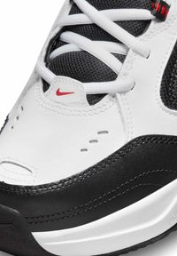 Sneaker in pelle bianca con accenti neri, lingua in mesh strutturato, lacci bianchi, dettaglio logo rosso e cuciture distintive sulla suola.