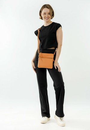 Pomarańczowa torba crossbody wykonana z teksturowanej skóry, z regulowanym paskiem i kieszeniami na zamek, w połączeniu z czarnym crop topem i czarnymi spodniami.