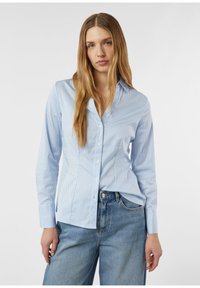 Light blue button-up shirt with vertical white stripes, long sleeves, and a pointed collar, paired with high-waisted denim jeans.