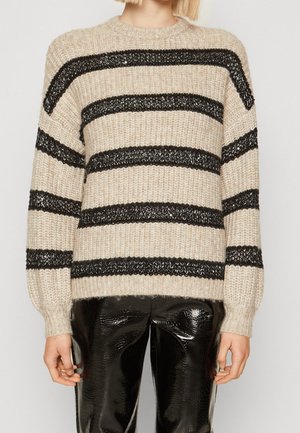 Pull en laine beige tricoté avec des rayures horizontales noires, présentant des poignets et un ourlet côtelés, associé à un pantalon noir à motifs brillants.