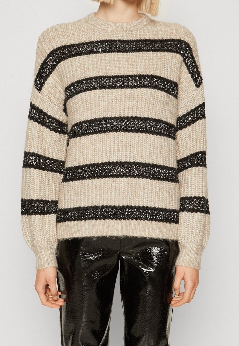 Beige stickad tröja med svarta horisontella ränder, med ribbade ärmslut och fåll, i kombination med blanka svarta mönstrade byxor.