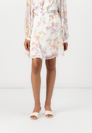 Jupe blanche à motifs floraux violet et orange, associée à un chemisier à manches longues assorti et des sandales beiges ouvertes à l'avant, portée par un mannequin.