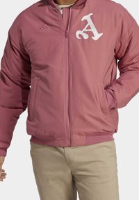 Rosa bomberjacka med dragkedja fram, ribbade ärm- och nederkanter, med en vit broderad bokstav 'A' och logotyp på vänster bröst.