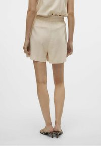 Ljusbeige shorts med resår i midjan, med en enkel design och mjuk textur. Bärs med transparenta klacksandaler.