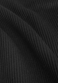 Schwarzer gerippter Stoff mit feinen vertikalen Linien, weicher Textur und subtiler Glanz. Das Material wirkt leicht und flexibel.