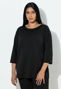 Czarna bluzka z długim rękawem z okrągłym dekoltem ozdobionym koralikami, wykonana z miękkiego materiału o luźnym kroju.