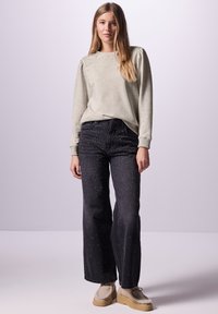 Pullover grigio chiaro a maniche lunghe con polsini a coste, abbinato a jeans scuri con borchie metalliche e scarpe piattaforme beige.