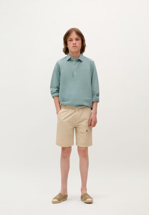 Hellblaues langärmliges Poloshirt, beige Shorts mit Taschen und beige Slipper. Glattes Material, lässige Passform und dezente Designdetails.