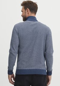 Suéter azul de punto con cuello alto, que presenta un patrón texturizado y puños y dobladillo acanalados. La longitud de las mangas es estándar. Se muestra la vista trasera.
