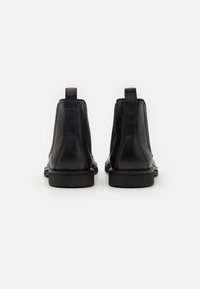 Botas de tobillo de cuero negro con un acabado liso, paneles laterales elásticos y una suela de goma baja. Cuentan con lengüetas en la parte trasera para facilitar su uso.