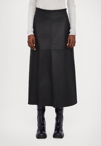 Schwarzer Midi-Rock aus Kunstleder mit hoher Taille, Nahtdetails und ausgestellter Form, kombiniert mit glänzenden schwarzen Stiefeletten.