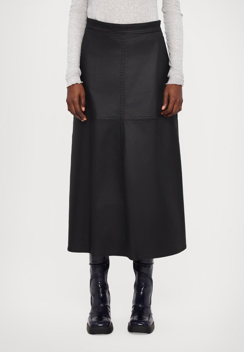 Schwarzer Midi-Rock aus Kunstleder mit hoher Taille, Nahtdetails und ausgestellter Form, kombiniert mit glänzenden schwarzen Stiefeletten.