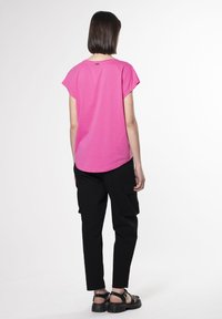 Korte roze t-shirt met korte mouwen en een ronde zoom, gecombineerd met zwarte cargobroeken en stevige zwarte sandalen.