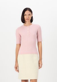 Rosa ribbad stickad topp med korta ärmar och rundad halsringning, med fem guldhjärtformade knappar. Matchad med en krämfärgad strukturerad blyertskjol.