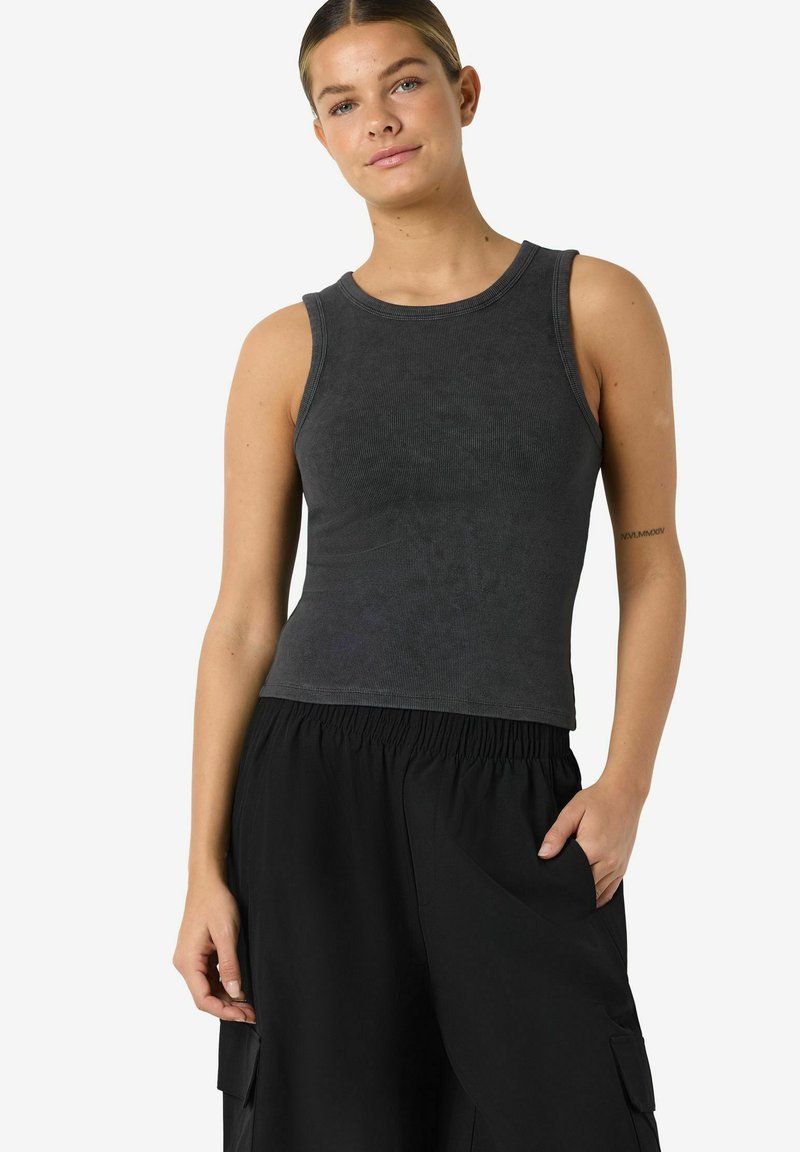 Sort ribbet tanktop med brede armhuller og rund halsudskæring, kombineret med løse sorte cargobukser med sidelommer.