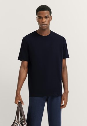 Navyblaues Kurzarm-T-Shirt aus weichem Material mit Rundhalsausschnitt und dezentem Branding auf der Brust. Getragen mit dunkelblauen Hosen.