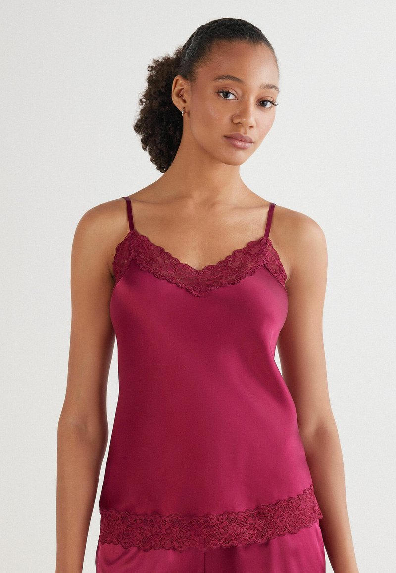 Bordeaux satijnen camisole met kantafwerking langs de halslijn en zoom, met dunne schouderbandjes en een zachte, gladde textuur.