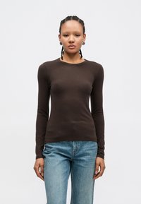 Καφέ μακρυμάνικο πουκάμισο από απαλό υλικό, με στρογγυλή λαιμόκοψη και εφαρμοστή γραμμή, συνδυασμένο με ανοιχτόχρωμο τζιν με διακριτικές λεπτομέρειες.