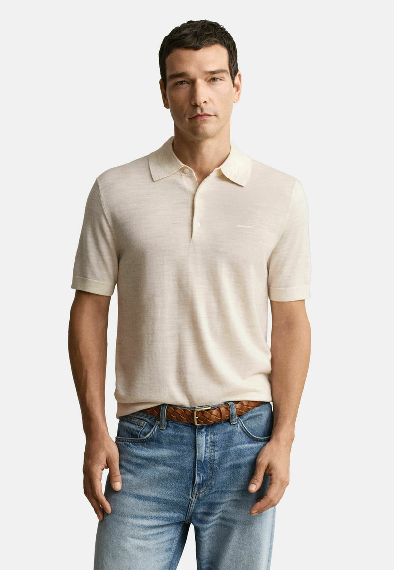 Beige polo shirt met korte mouwen, van een zachte stof en met een klassieke kraag, gecombineerd met lichtblauwe denim jeans en een bruine gevlochten riem.