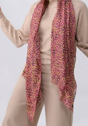 Tenue beige avec une longue écharpe rose et marron à pois, portée lâchement autour du cou, par-dessus un pull à col roulé et un pantalon.