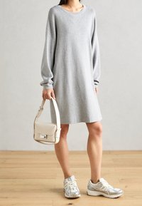 Robe grise en maille à manches longues avec un col rond, assortie à des baskets argentées et blanches ainsi qu'à un sac à main beige au design structuré.